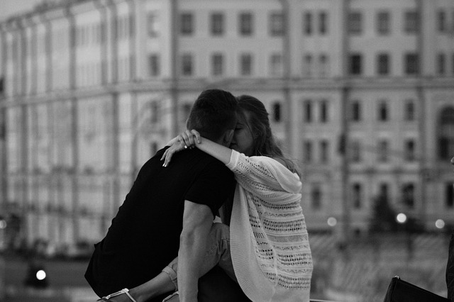 Černobílá fotografie ve městě, uprostřed je zamilovaný pár, který se líbá